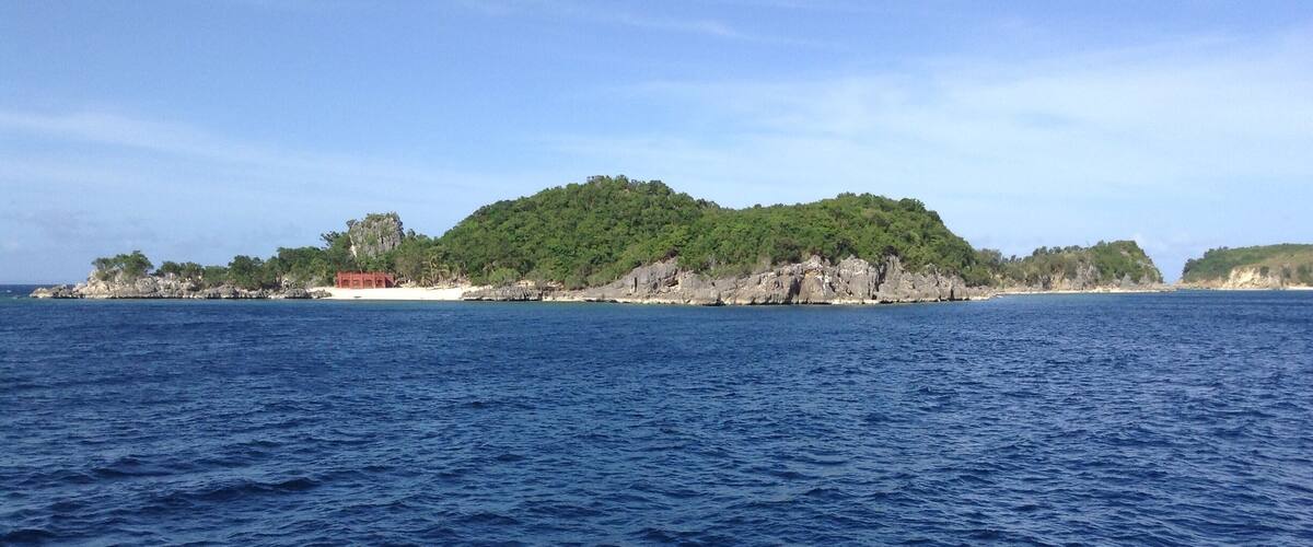 A coastal landscape with a rocky island covered in greenery and a clear blue sea.