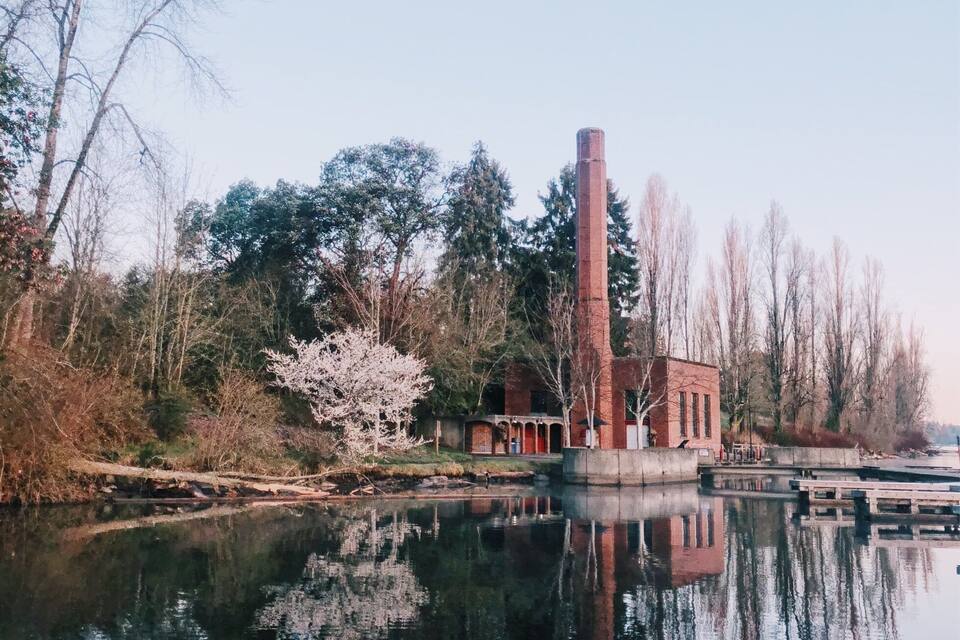 A calm river reflecting a brick building and trees.