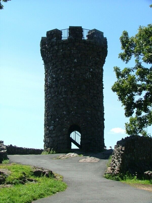 A stone tower with a gate, surrounded by greenery and a clear sky.
