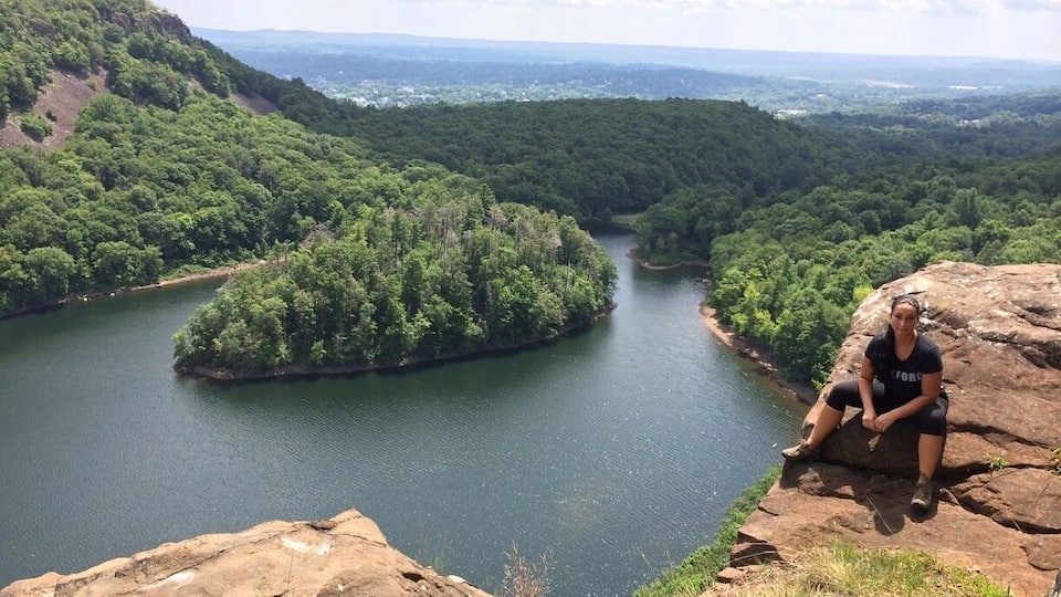 A person sitting on a rock overlooking a river surrounded by dense forest.