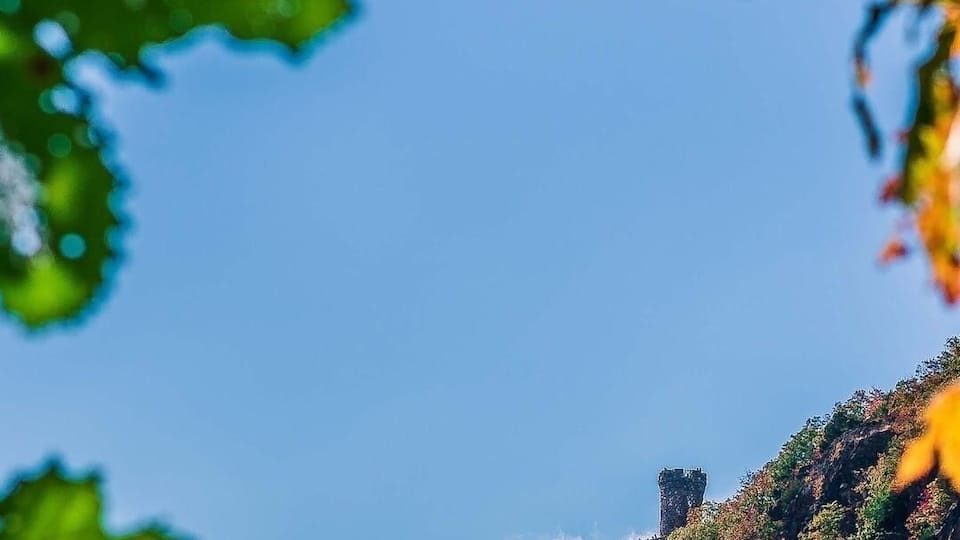 A mountain with autumn foliage and a castle-like structure on top.