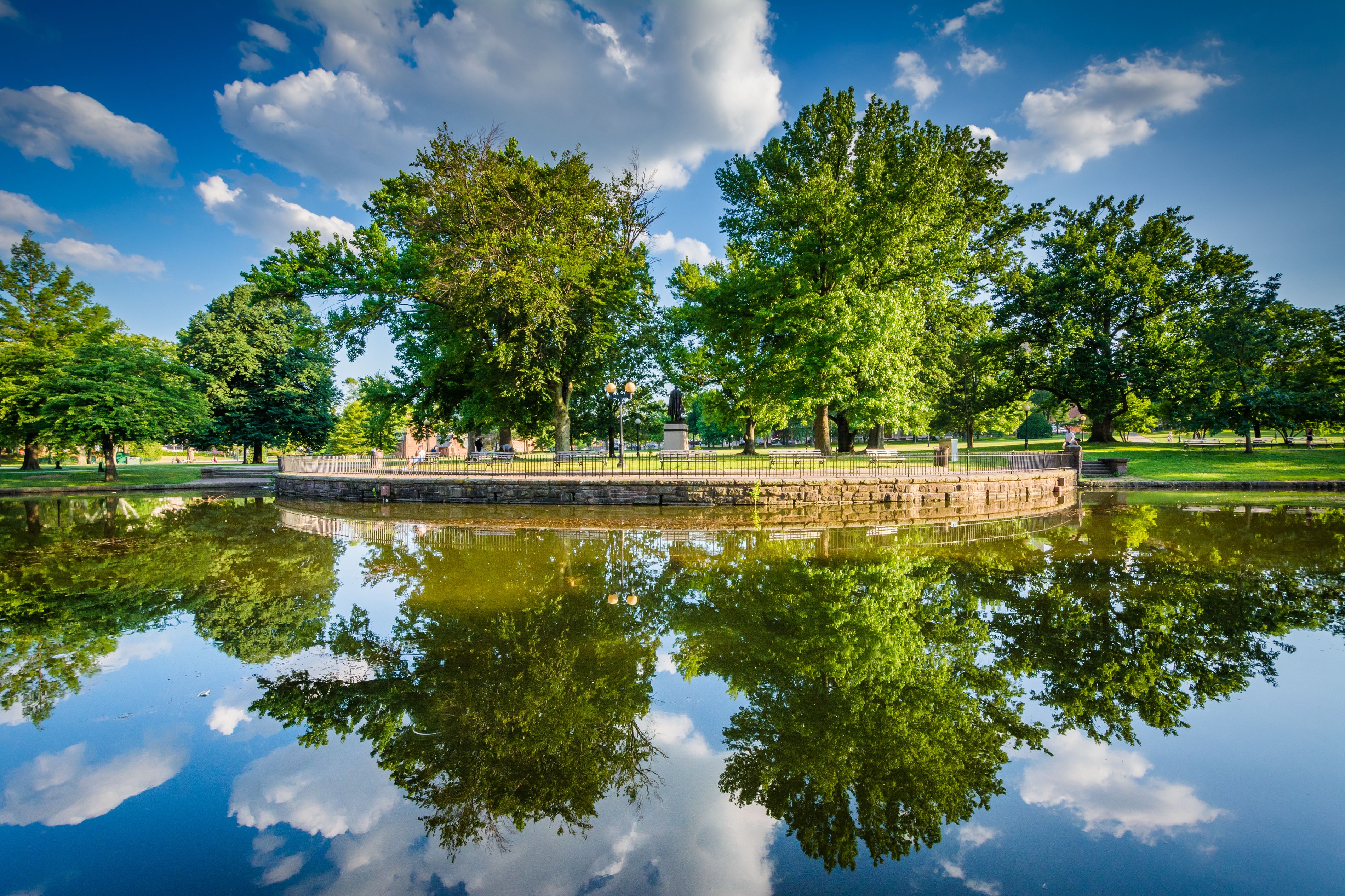 A serene park with a reflective pond, lush trees, and a stone wall.