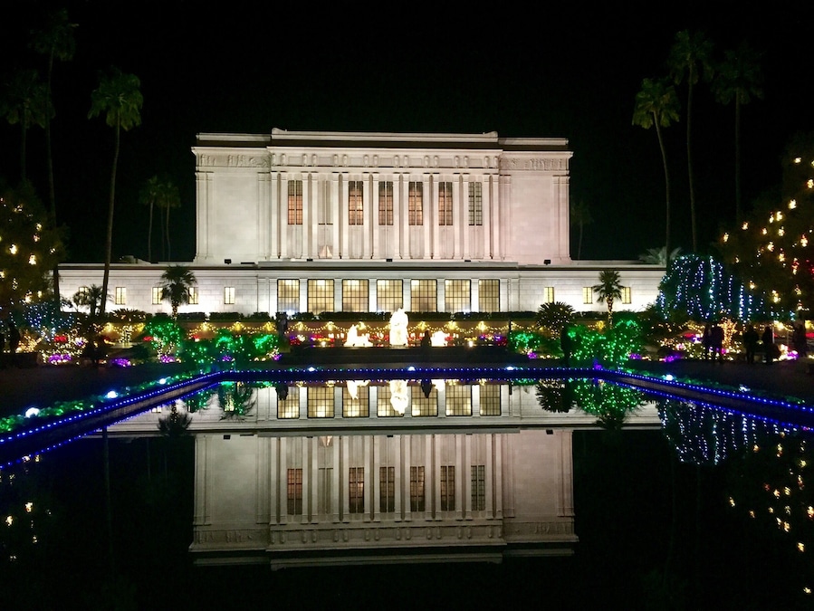 Um edifício imponente com arquitetura clássica, iluminado por luzes festivas e refletido em um espelho d'água.