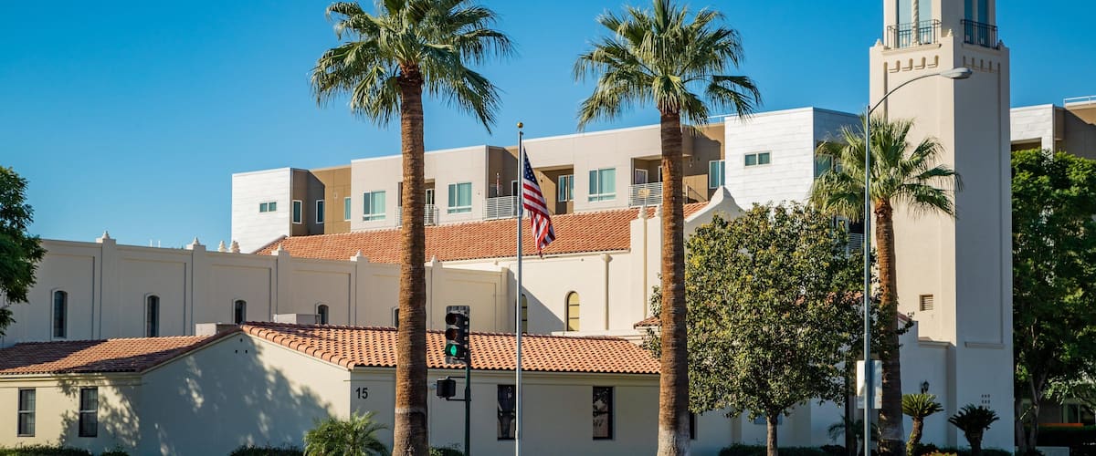 A building with a red-tiled roof, palm trees, and a flagpole with an American flag.