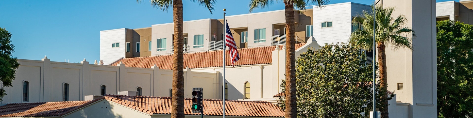 A building with a red-tiled roof, palm trees, and a flagpole with an American flag.