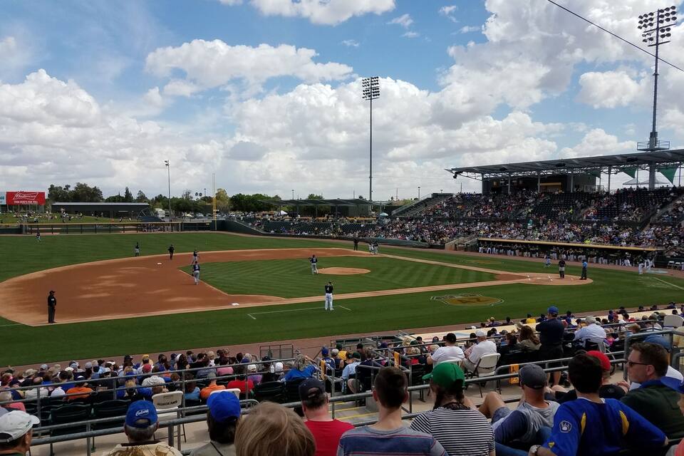 A baseball stadium with a green field, a crowd of spectators, and a clear sky with clouds.