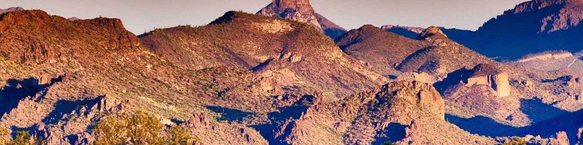 A rugged mountain range with a prominent peak, sparse vegetation, and a clear sky.