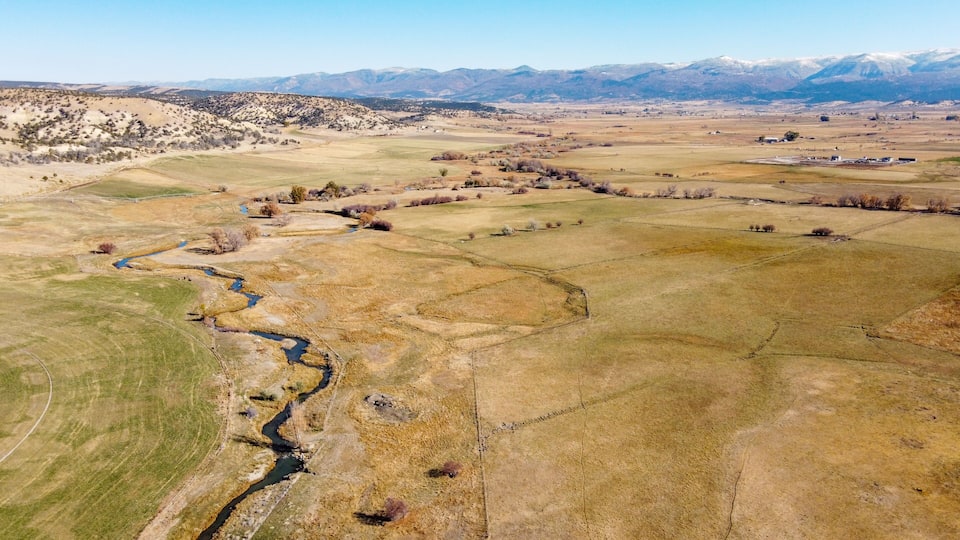 A vast landscape with a river meandering through fields, distant mountains, and sparse vegetation.