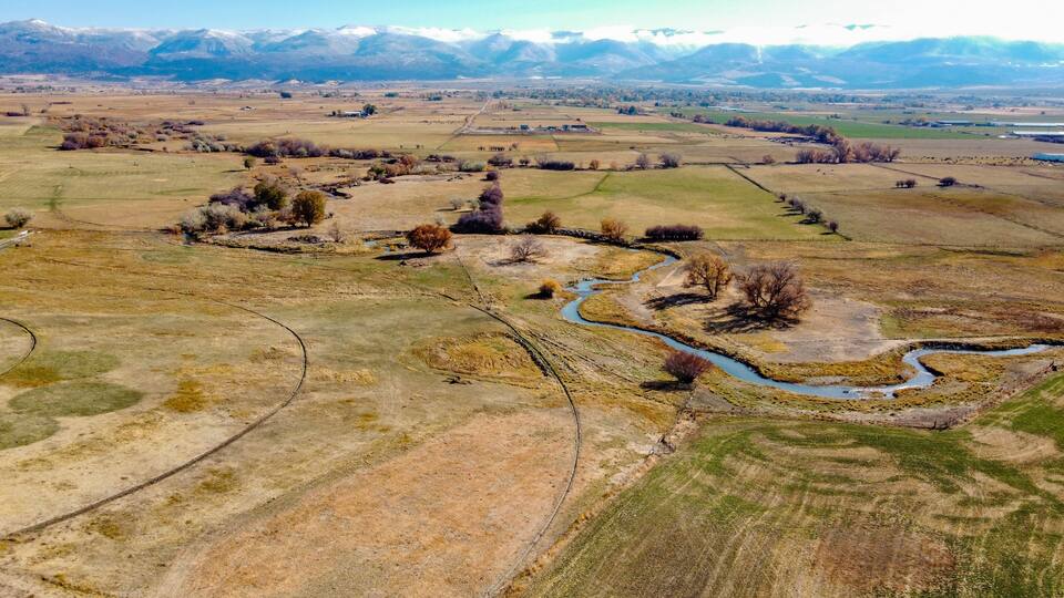 A river winding through a valley with fields and sparse trees, surrounded by distant mountains.