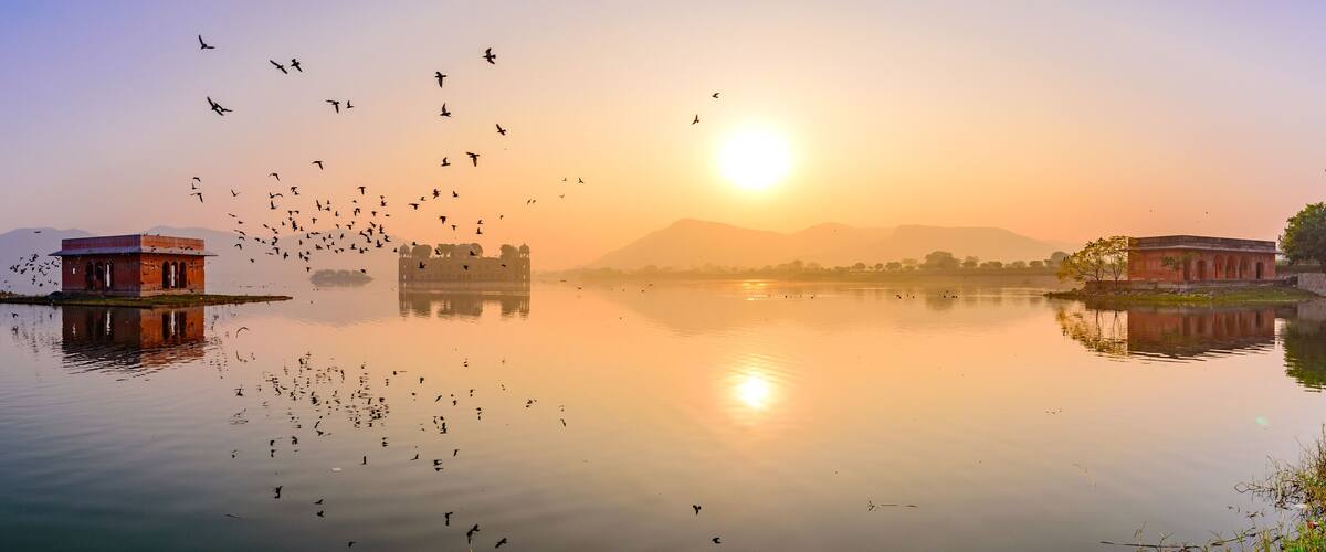 A calm lake with a sunset, a tower, and a palace in the background.