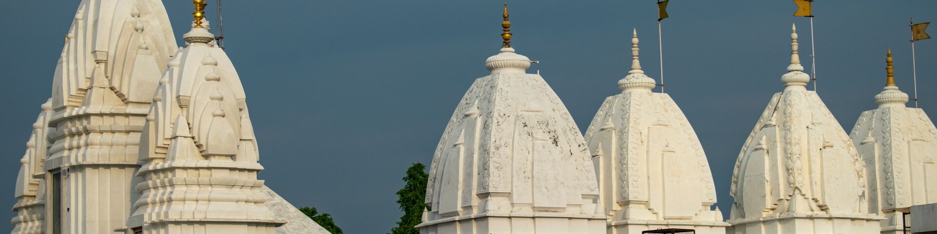 A magnificent white temple with intricate domes and golden spires, adorned with yellow flags, standing against a clear blue sky.The serene structure of jain temples in Hastinapur, uttar pradesh india.