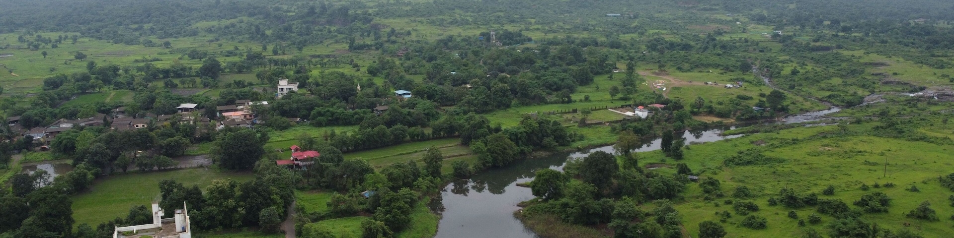 A river flowing through a green valley with a prominent mountain in the background and a small settlement with buildings near the riverbank.