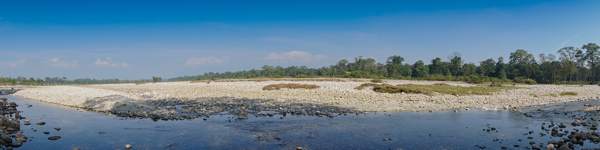 Panoramic view of Murti river, riverbed in foreground with flowing water and stones. Scenic beauty of Dooars landscape, West Bengal, India