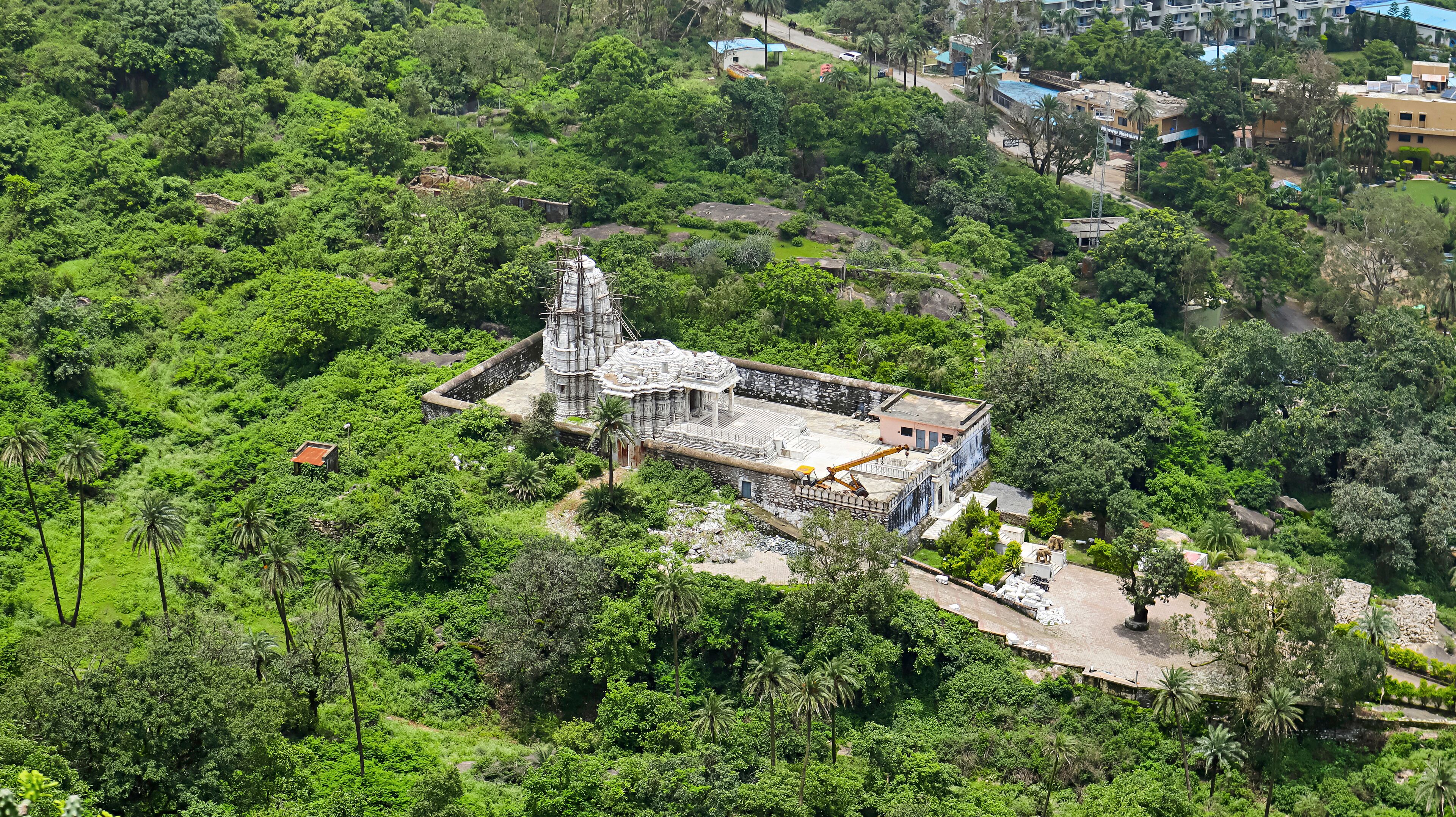 An ancient temple surrounded by dense greenery and modern buildings.