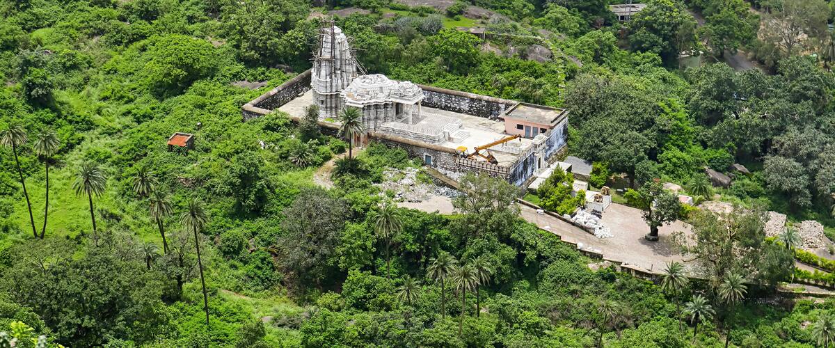 An ancient temple surrounded by dense greenery and modern buildings.