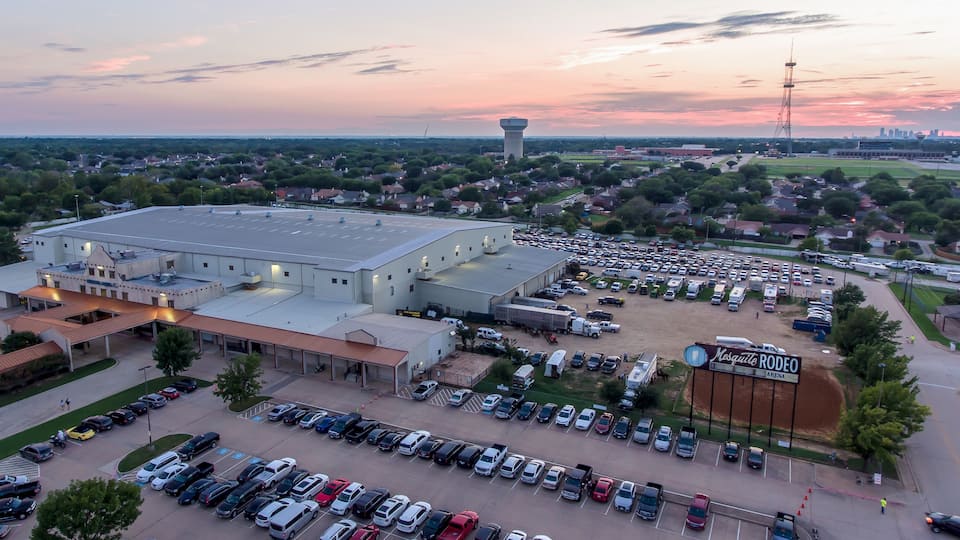 A large parking lot, a stadium, and a city skyline at dusk.