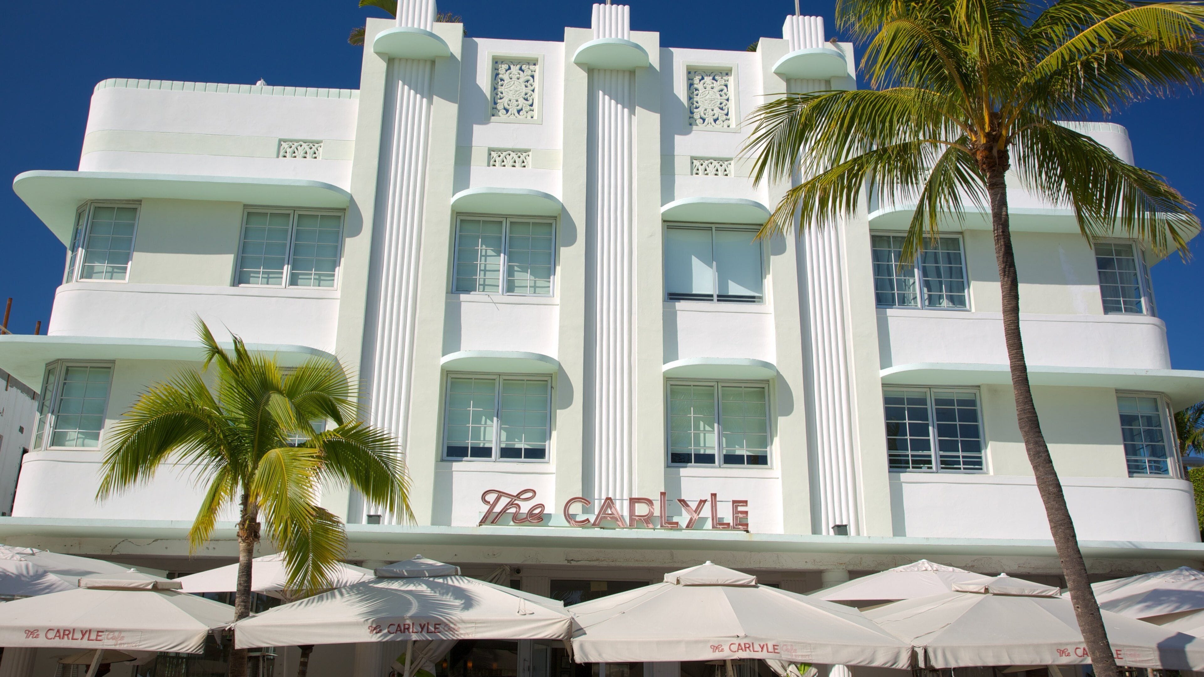 The Carlyle hotel with white columns and palm trees in front.