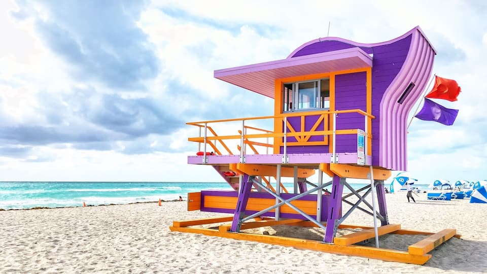 Una torre de salvavidas en una playa, con cielo despejado y el océano al fondo.
