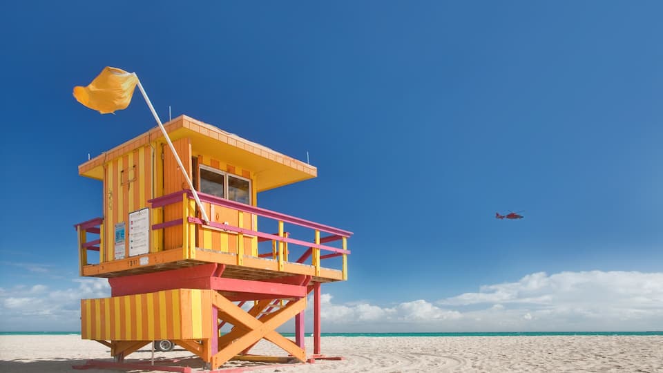 A lifeguard tower on a beach with a helicopter in the sky.
