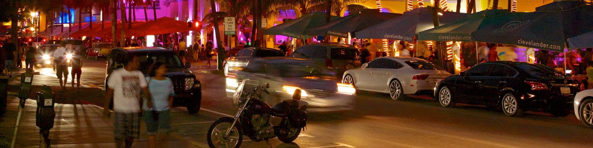 A busy street at dusk with palm trees, cars, and illuminated buildings.