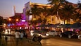 A busy street at dusk with palm trees, cars, and illuminated buildings.