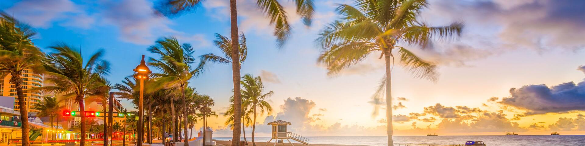 A beach with palm trees, a lifeguard tower, and a sunset.