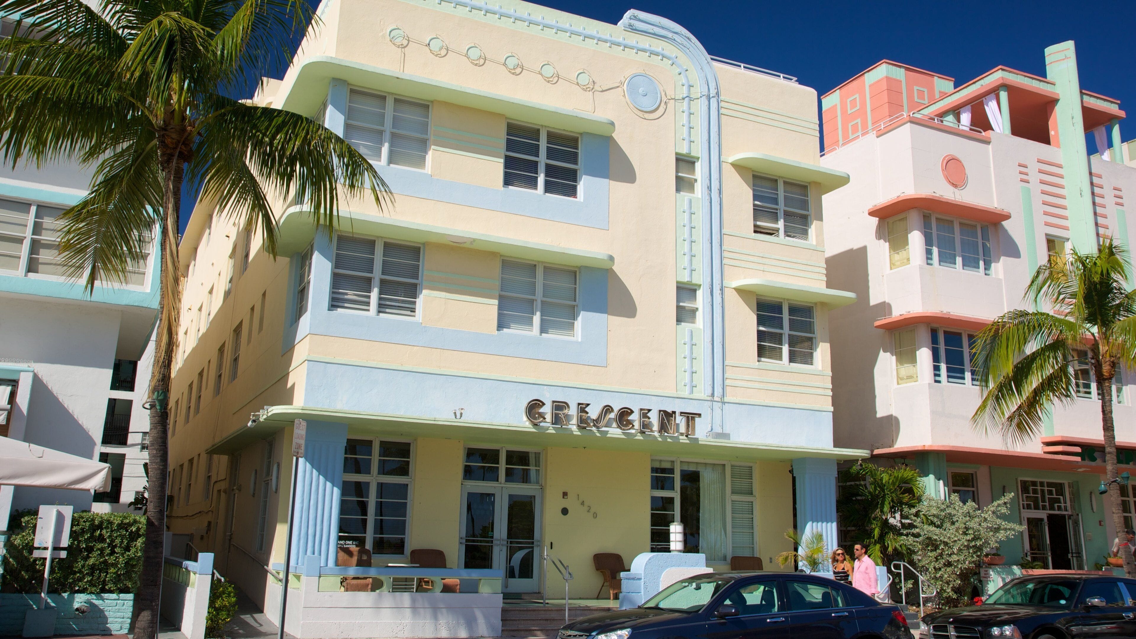 A vintage building with the name 'Crescent' on the facade, palm trees, and parked cars.