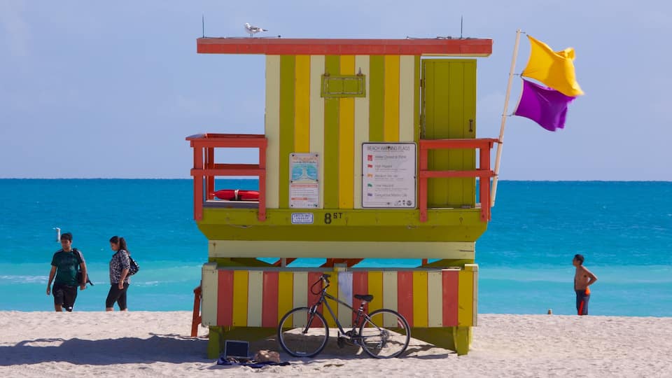 A lifeguard tower with a yellow and red striped design, a flag, and a sign indicating beach warnings.