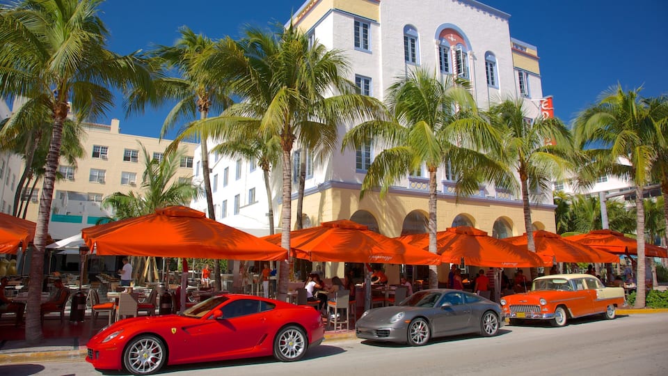 A red sports car, a gray sports car, and a vintage orange car parked on a street with palm trees and orange umbrellas.