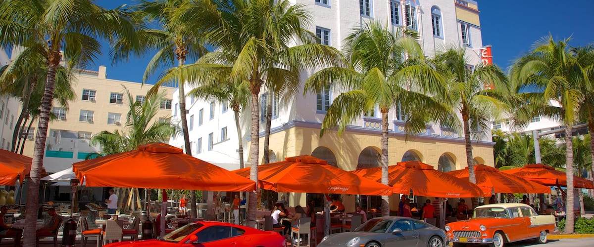 A red sports car, a gray sports car, and a vintage orange car parked on a street with palm trees and orange umbrellas.