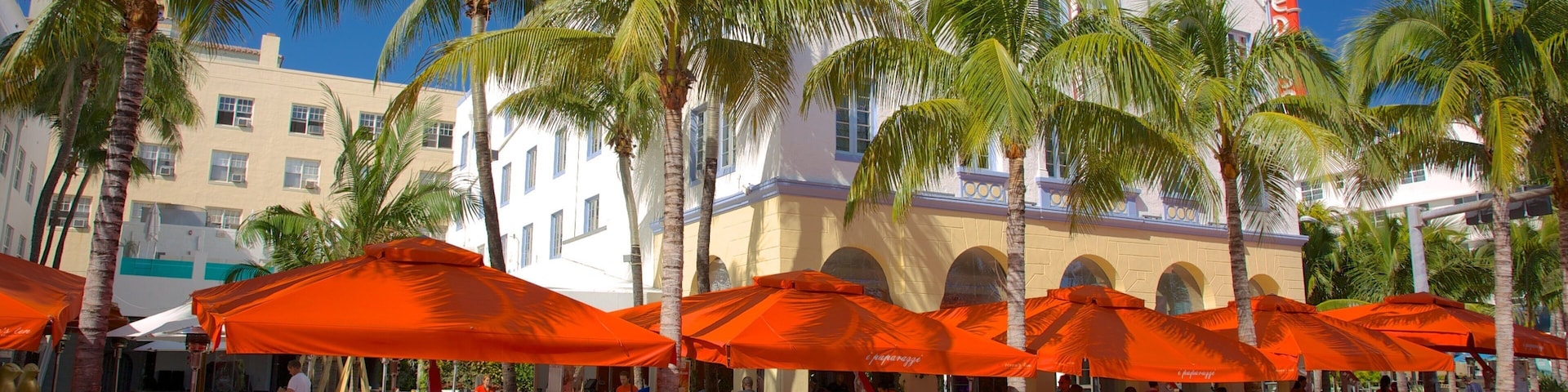 A red sports car, a gray sports car, and a vintage orange car parked on a street with palm trees and orange umbrellas.