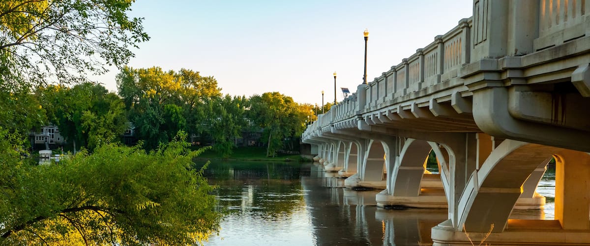 A bridge over a calm river with lush greenery and trees on both sides.