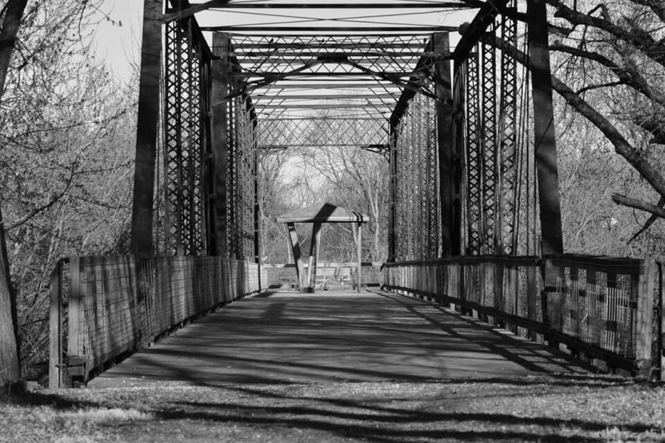 A metal bridge with a wooden walkway, surrounded by trees.