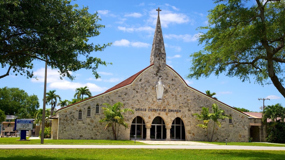 A stone church with a cross on top, surrounded by trees and a clear sky.