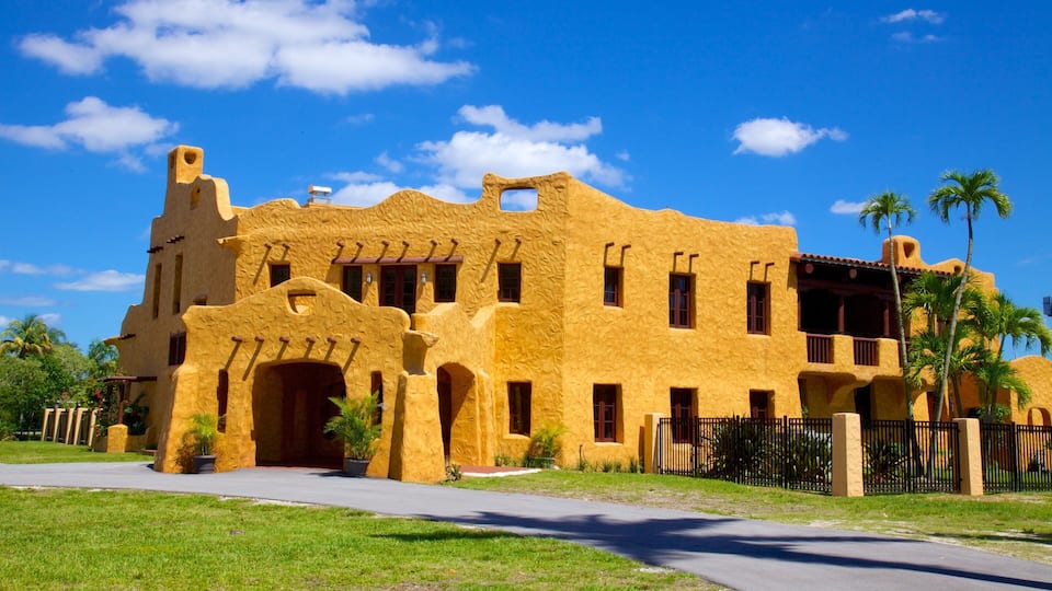 A large, yellow building with a unique architectural style, surrounded by palm trees and a clear blue sky.