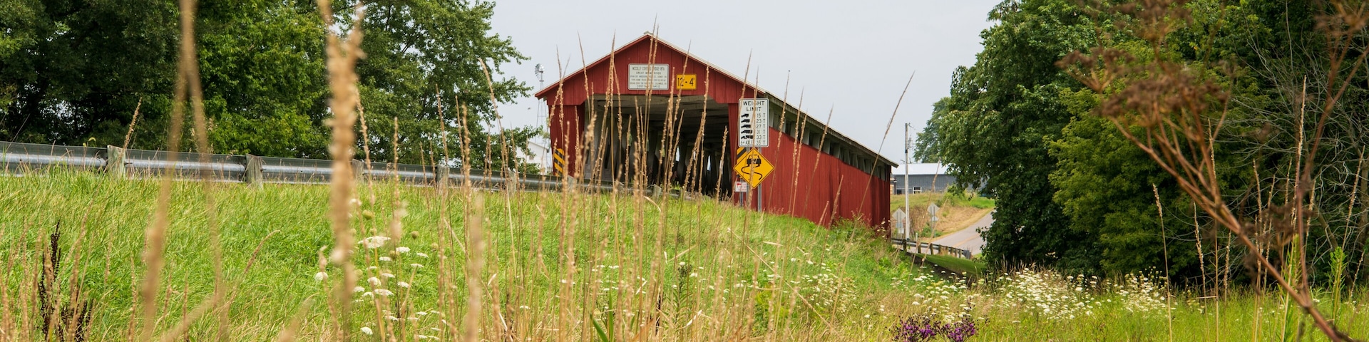 A red barn with a weight limit sign, surrounded by lush greenery and wildflowers.