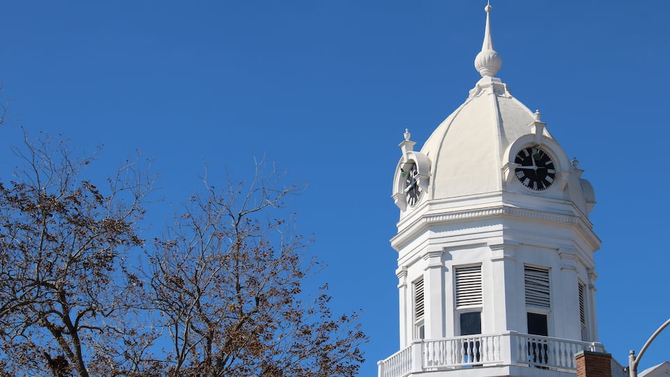 A white clock tower with a dome and a spire against a clear blue sky.