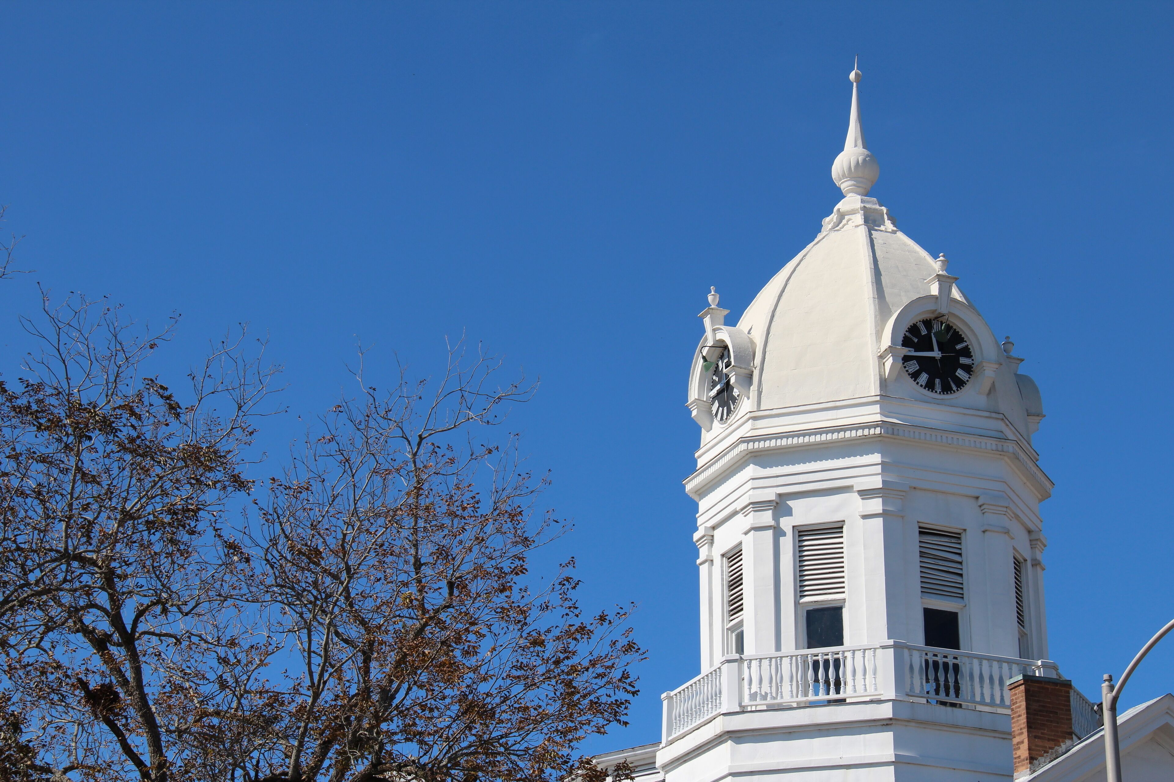 A white clock tower with a dome and a spire against a clear blue sky.