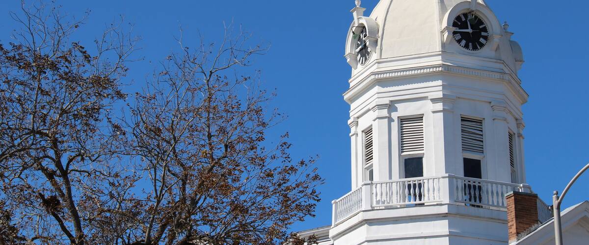 A white clock tower with a dome and a spire against a clear blue sky.