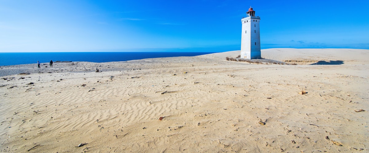 A white lighthouse on a sandy beach with the ocean in the background.