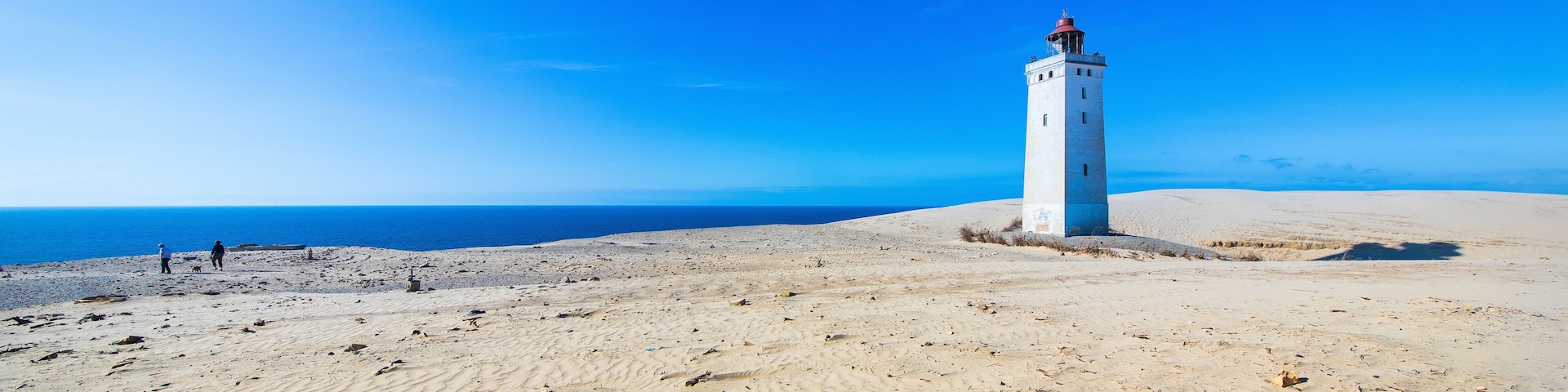 A white lighthouse on a sandy beach with the ocean in the background.