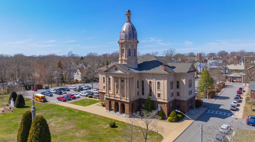A large, historic building with a prominent dome and tower, surrounded by a parking lot and a grassy area with trimmed bushes.