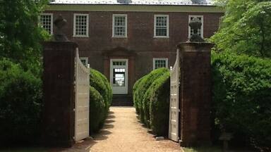 A brick building with a gated entrance, a gravel path, and trimmed hedges.