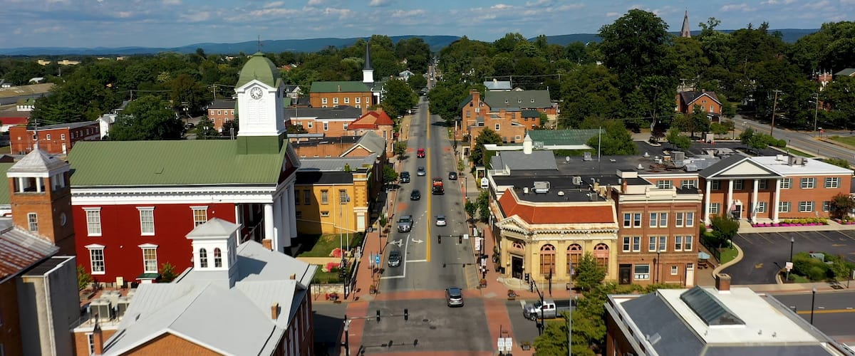 A town with a prominent clock tower, a green-roofed building, and a street lined with variously colored buildings.