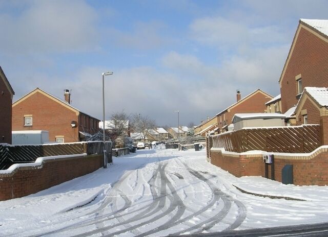 A snow-covered residential street with houses on both sides.