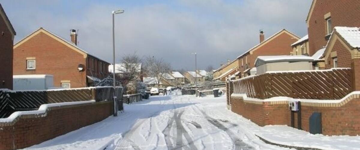 A snow-covered residential street with houses on both sides.