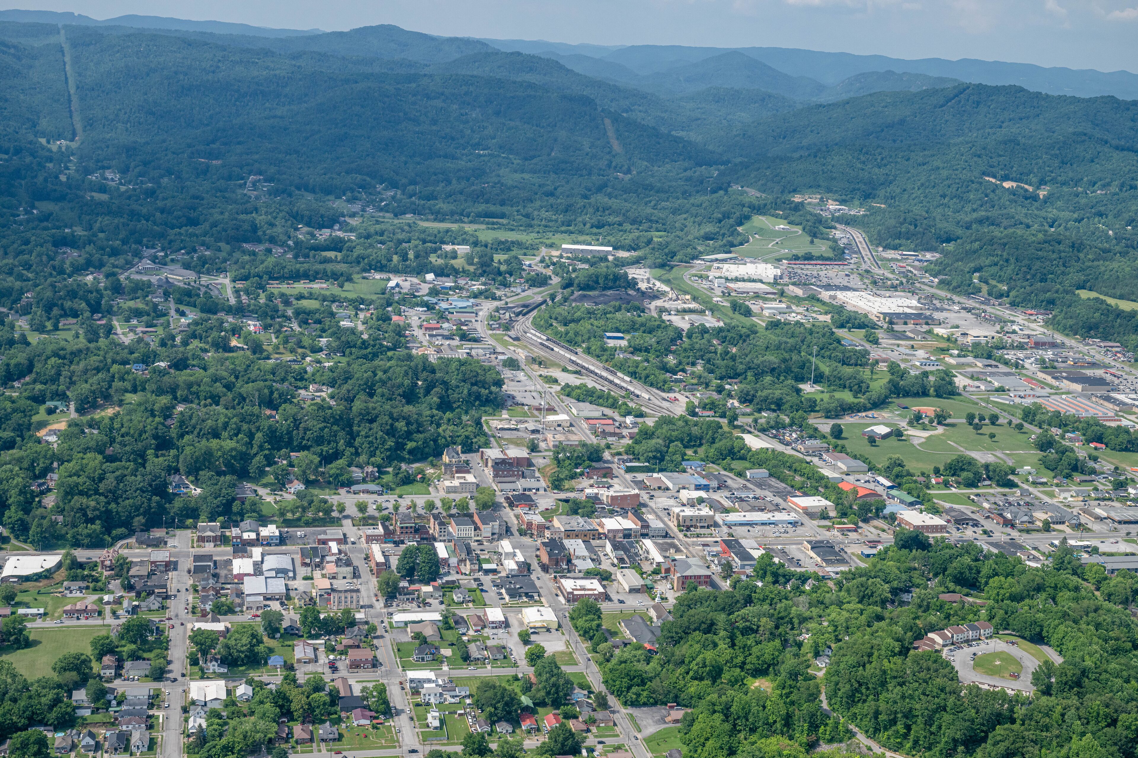An aerial view of a town surrounded by mountains, with a mix of residential and commercial buildings, and a highway running through the center.