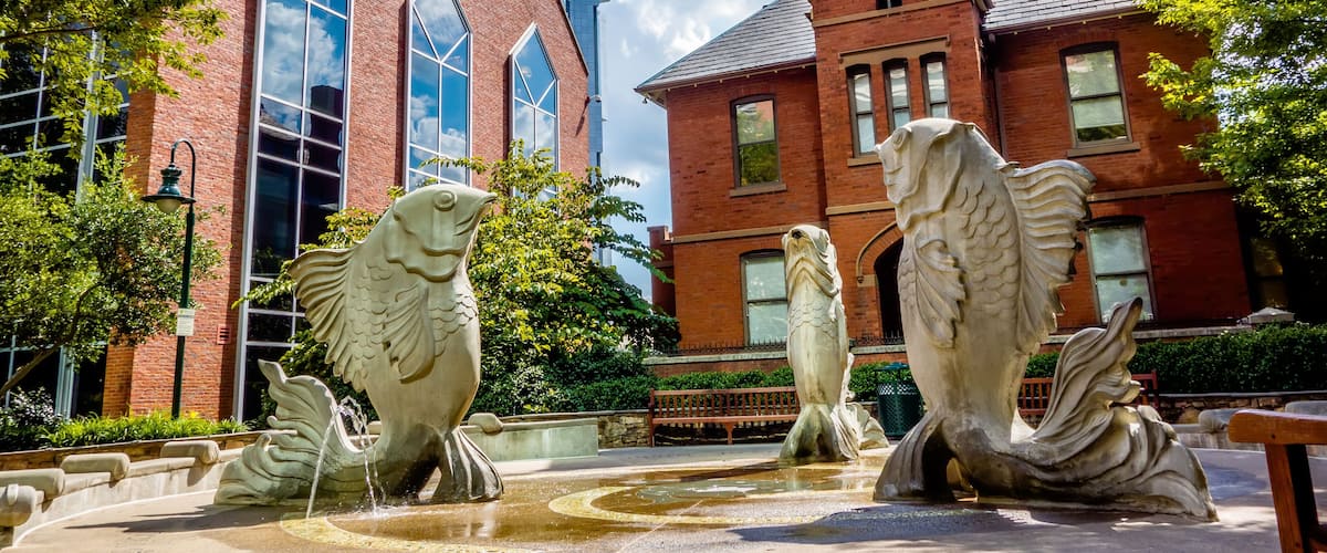 A building with large windows and a fountain with fish sculptures.
