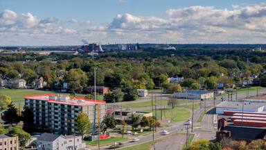 Aerial view of a vibrant cityscape where building contrasts with the lush green trees, leading to distant industrial structures under a dynamic sky, Middletown, Ohio, United States.