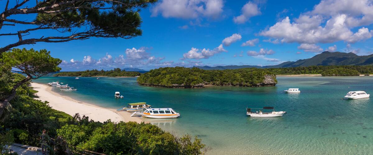 Glass bottom boats in the tropical lagoon beach with clear blue water and white sand in Kabira bay, Yaeyama Islands, Ishigaki, Japan